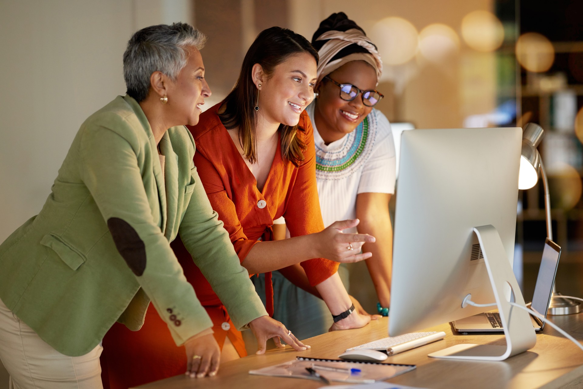 Computer, business and a female leader with her team, working overtime together in the office at night. Collaboration, diversity and coaching with a senior woman manager training her staff at work